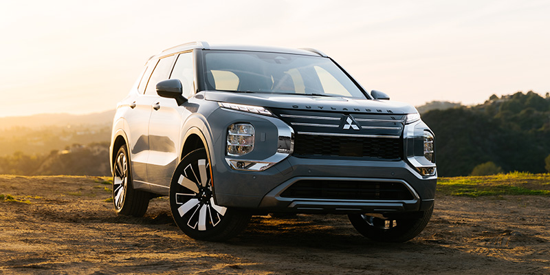 Front-three-quarter view of a silver Mitsubishi Outlander parked on a dirt hill at sunset.