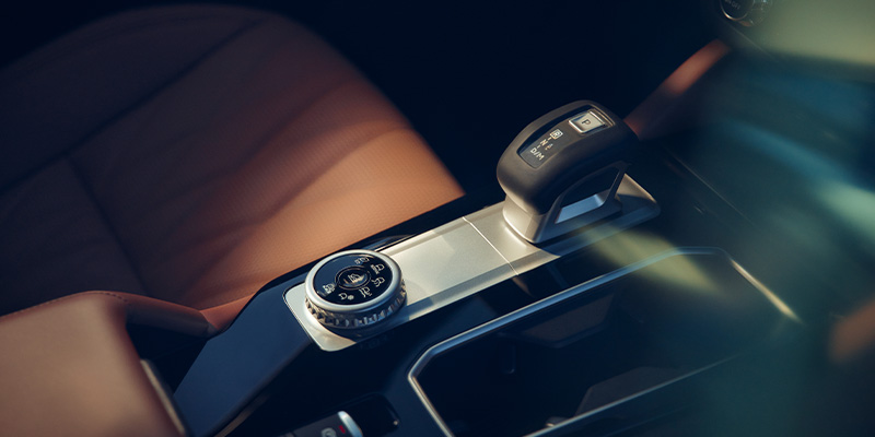 Close-up view of the center console featuring an electronic gear shifter and drive mode dial next to a tan leather seat.